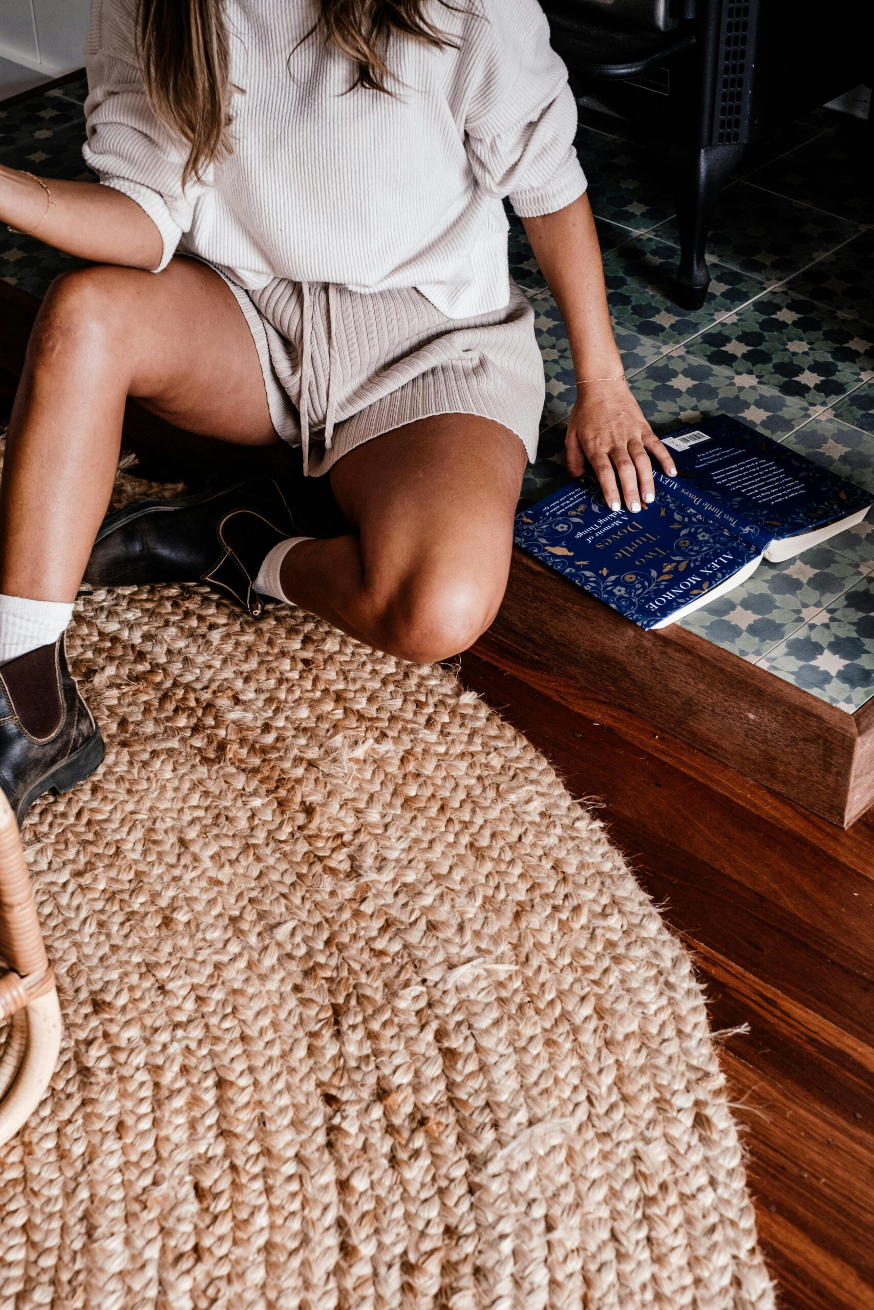 Fashionable woman sitting with a book on a textured rug, showcasing modern style.